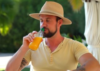 un homme avec un chapeau en vacances a chaud et boit à la bouteille